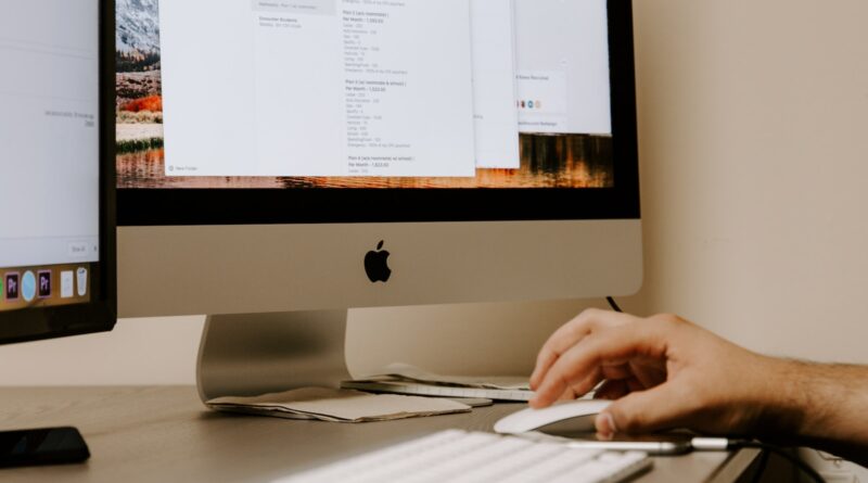 person holding white Apple Magic Mouse beside iMac and keyboard